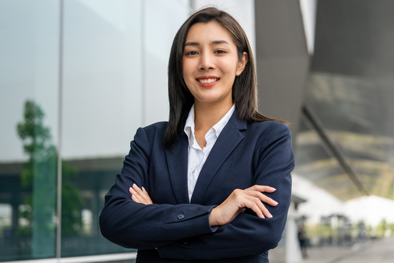 Confident woman in a business suit standing in front of a modern glass building, representing leadership and career advancement through legal education.
