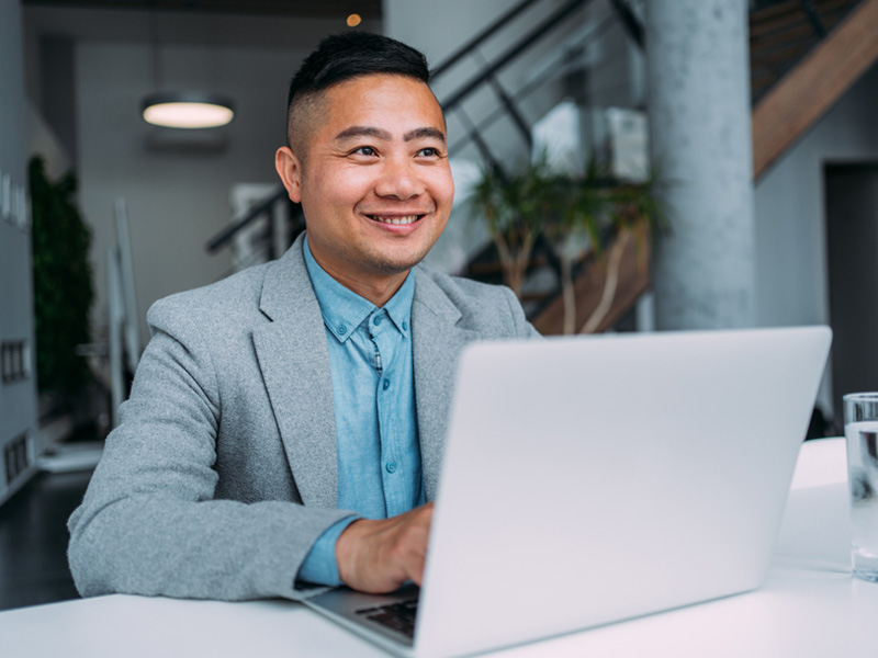 Smiling professional using a laptop, illustrating the flexibility and convenience of online legal studies for working adults.